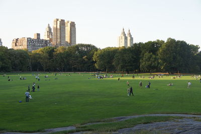 People playing soccer on field against sky in city