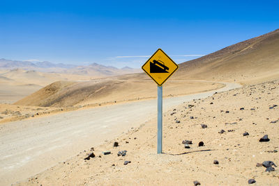 Road sign on desert against clear blue sky