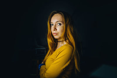 Portrait of young woman standing against black background