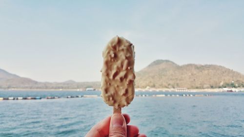 Close-up of hand holding ice cream against sea