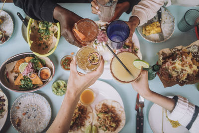 Directly above view of hands toasting glass of fresh cocktails while celebrating at restaurant