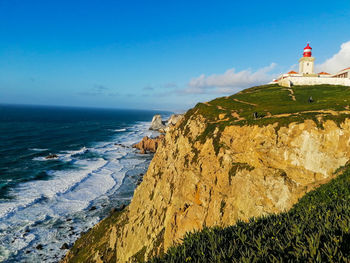 Lighthouse on beach by sea against sky