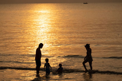 Silhouette family enjoying in sea during sunset