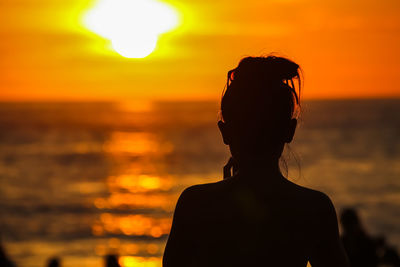 Rear view of silhouette woman standing at beach during sunset