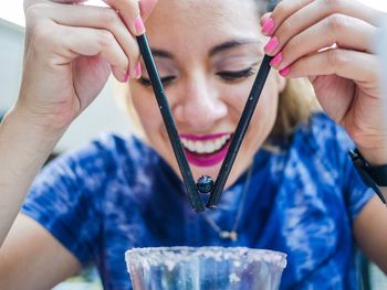 Happy woman picking up blueberry with drinking straws over glass