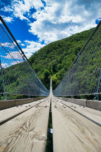 Empty footbridge amidst trees against sky