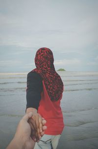 Rear view of woman holding hands with man on beach against sky