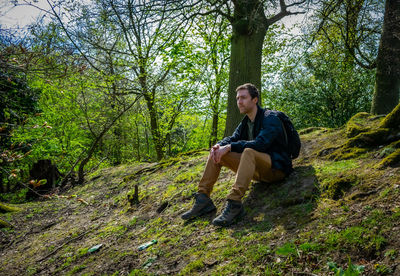 Low angle view of young man sitting on hill in forest