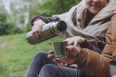 Woman pouring water from thermos by man in forest