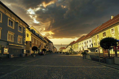 Street amidst buildings against sky during sunset