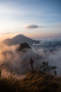 Silhouette man standing on cliff against mountains during sunset