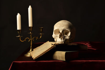 Close-up of human skull on book by candles at table against black background