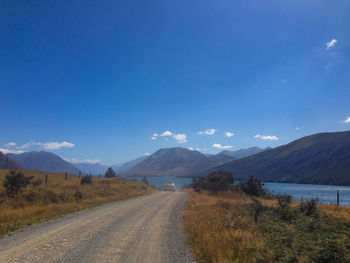 Road leading towards mountains against blue sky