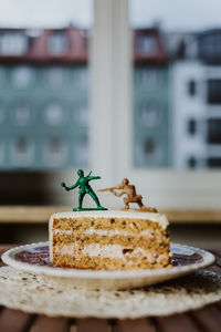 Two toy soldiers fighting on the top of a piece of cake - close up window in background