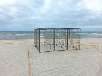 Cage at beach against cloudy sky