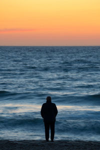 Rear view of man standing on beach during sunset