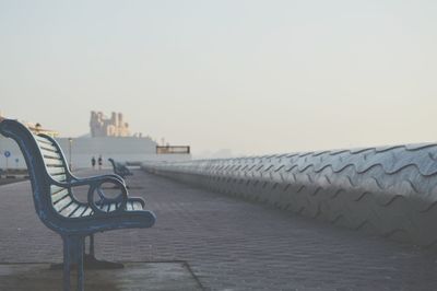 Empty metallic bench on promenade against clear sky