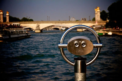 Coin-operated binoculars by river in city against sky