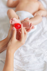 Mother holds newborn baby feet. tiny fingers, red massage ball in woman hand. cozy morning at home.