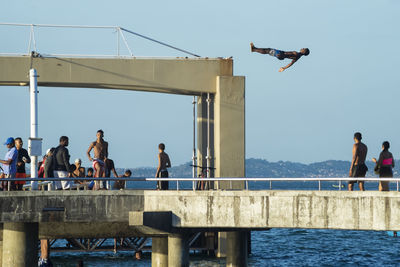 People jumping on bridge over sea against clear sky