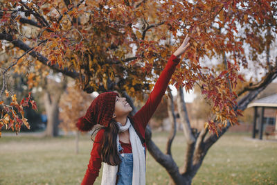Young woman standing by tree in park during autumn