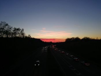 Highway amidst trees against sky during sunset