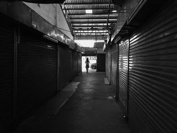 Rear view of woman walking in alley amidst closed shops