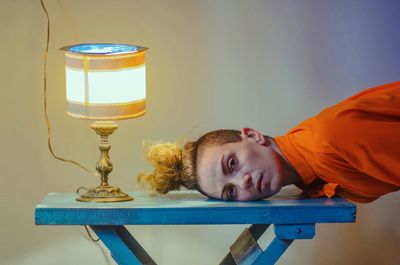 Portrait of woman with head down on table by lamp at home