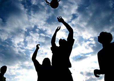 Silhouette people playing with basketball against sky