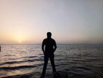 Rear view of silhouette man standing at beach during sunset