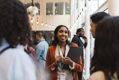 Smiling female entrepreneur holding folder and discussing with delegates during seminar at convention center