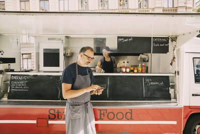 Mature chef using mobile phone against street food truck