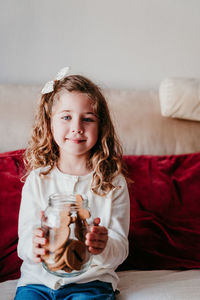 Portrait of girl holding food in container while sitting on sofa at home