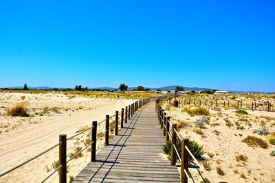 Footpath leading to wooden wall against clear blue sky