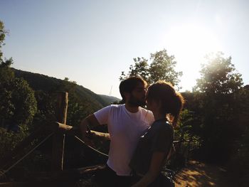 Couple kissing by railing against clear sky