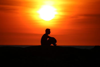 Silhouette man sitting on land against sky during sunset