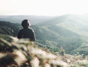 Rear view of young man standing on landscape against sky