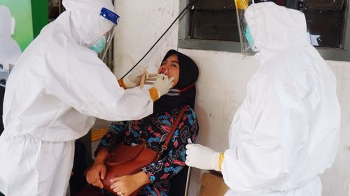 Doctors wearing protective suit examining patient while sitting outdoors