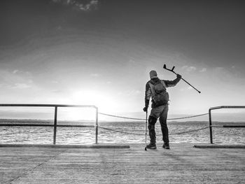 Traveler with backpack walk difficulty with medicine poles. hurt tourist on bridge near sea. bw