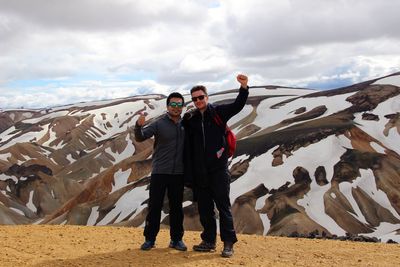 Full length of man with friend showing thumbs up sign against mountain during winter