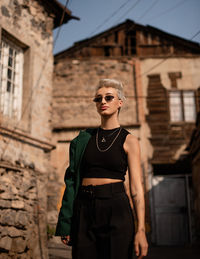 Portrait of young woman wearing sunglasses while standing against building