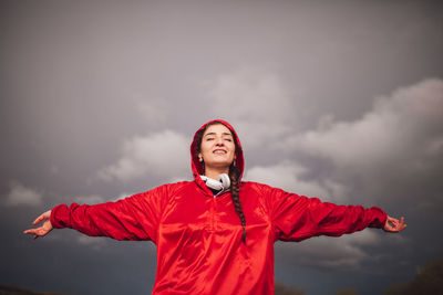 Young woman with arms outstretched standing against sky