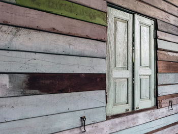 Old grunged wooden window frame painted white vintage with old colourful plywood wall. 