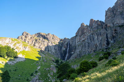 Low angle view of rocky mountains against clear blue sky