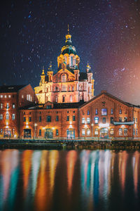 Illuminated buildings by river against sky at night