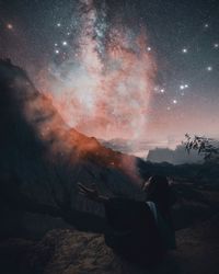 Rear view of woman sitting on land against sky at night