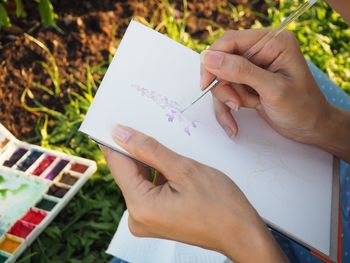 High angle view of woman hand painting on paper in park