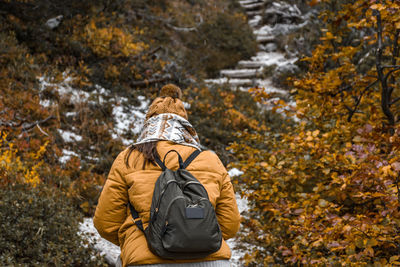 Rear view of young woman wearing yellow winter jacket, hiking on path in autumn woods