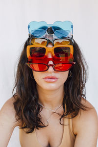 Young woman wearing various sunglasses in front of white wall