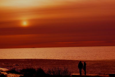 Silhouette people on beach against orange sky